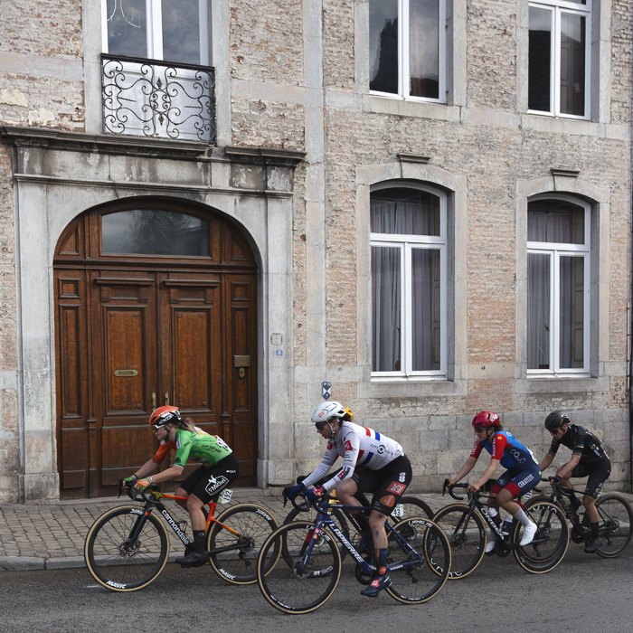 La Flèche Wallonne Femmes 2025 - Riders pass the large arched wooden door of a grand building in Huy