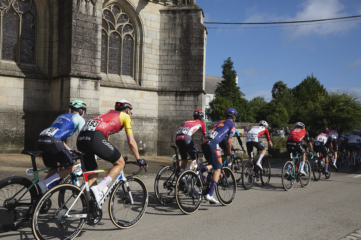 Bretagne Classic - Ouest-France 2025 - The peloton passes in front of the church in Kernascléden