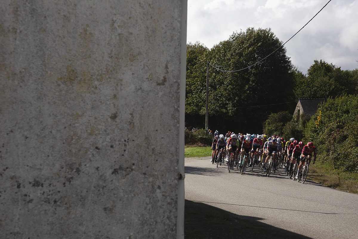 Bretagne Classic - Ouest-France 2025 - Riders are framed by the side of a house as they pass through Kersamuel