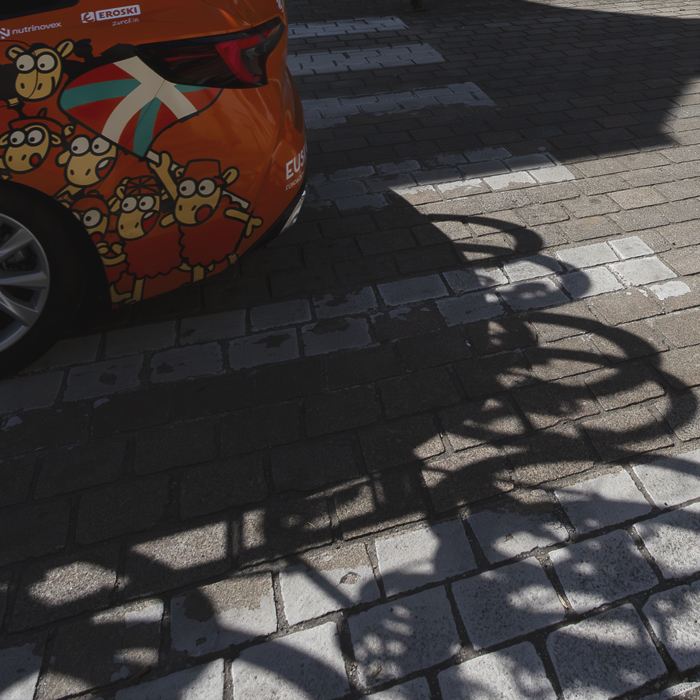 Bretagne Classic - Ouest-France 2025 - Shadows of bikes are cast on the road from the Euskaltel - Euskadi team car on which Cartoon sheep are depicted waving the Basque flag