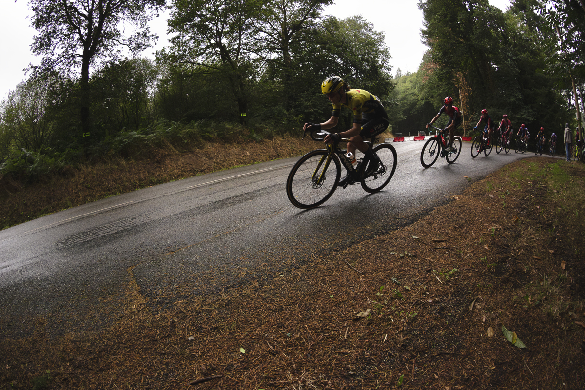 Classic Lorient Agglomération - Ceratizit 2025 - A string out group of riders pass down a road littered with fallen pine needles from the surrounding woodland