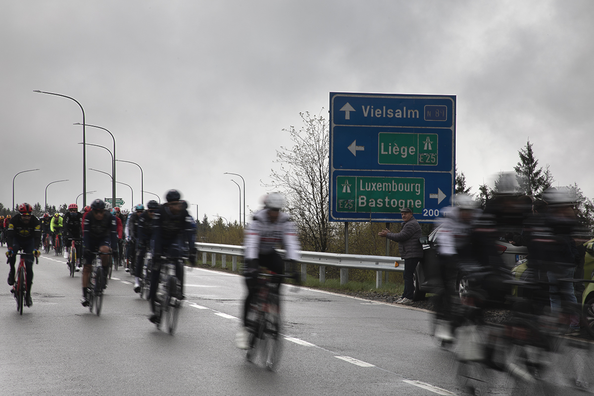 Liège-Bastogne-Liège 2024 - Riders speed past a sign pointing to Liege and Bastogne at Baraque Fraiture