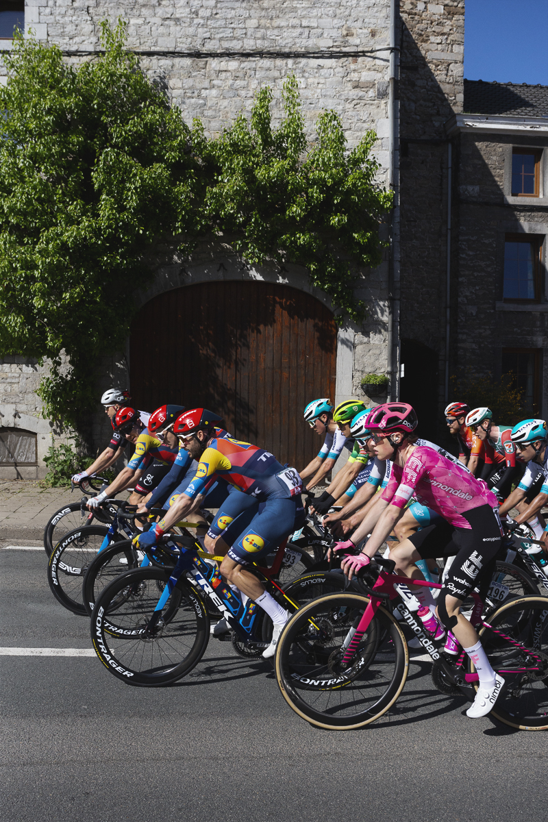 Liege Bastogne Liege 2025 - The peloton passes in front of an arched barn door in Harzé