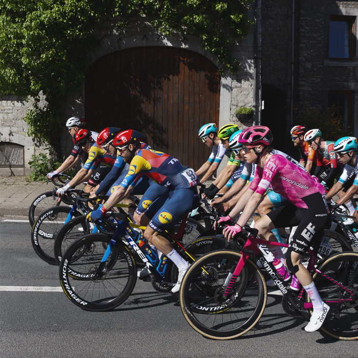 Liege Bastogne Liege 2025 - The peloton passes in front of an arched barn door in Harzé