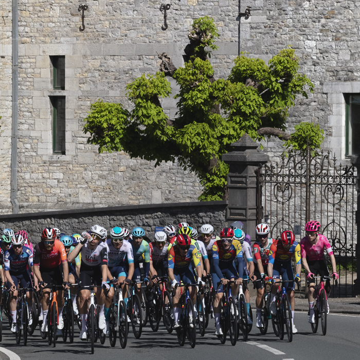 Liege Bastogne Liege 2025 - A stone wall of Château de Harzé looms in the background as the riders pass its iron gates