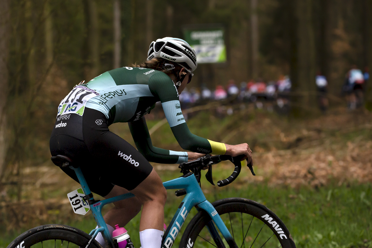 Liège-Bastogne-Liège Femmes 2023 - Lifeplus Wahoo’s Ella Harris climbs through the woodland with the peloton visible through the trees in front