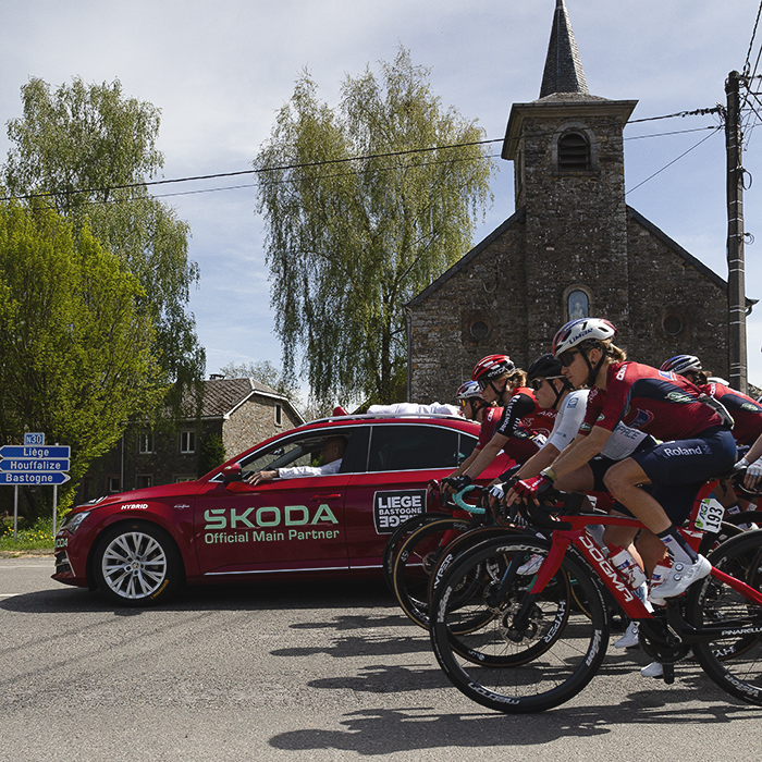 Liège Bastogne Liège Femmes 2025 - Riders line up behind the Race Director’s car, a church and sign reading Liege and Bastogne in the background during the neutralised start
