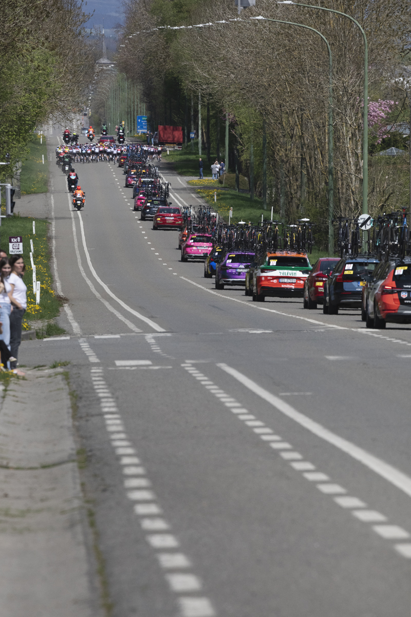 Liège Bastogne Liège Femmes 2025 - The race convoy lines out down a long straight road with riders in the distance in Foy
