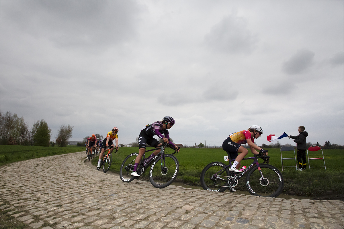 Paris Roubaix Femmes 2023 - Riders round a corner as a child waves a tricolour from the side of the race