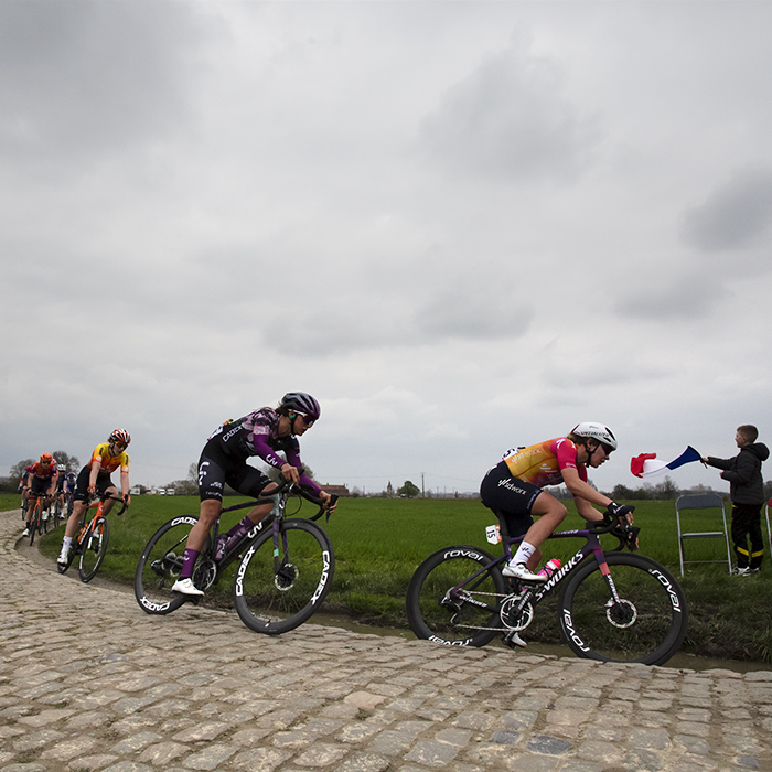 Paris Roubaix Femmes 2023 - Riders round a corner as a child waves a tricolour from the side of the race