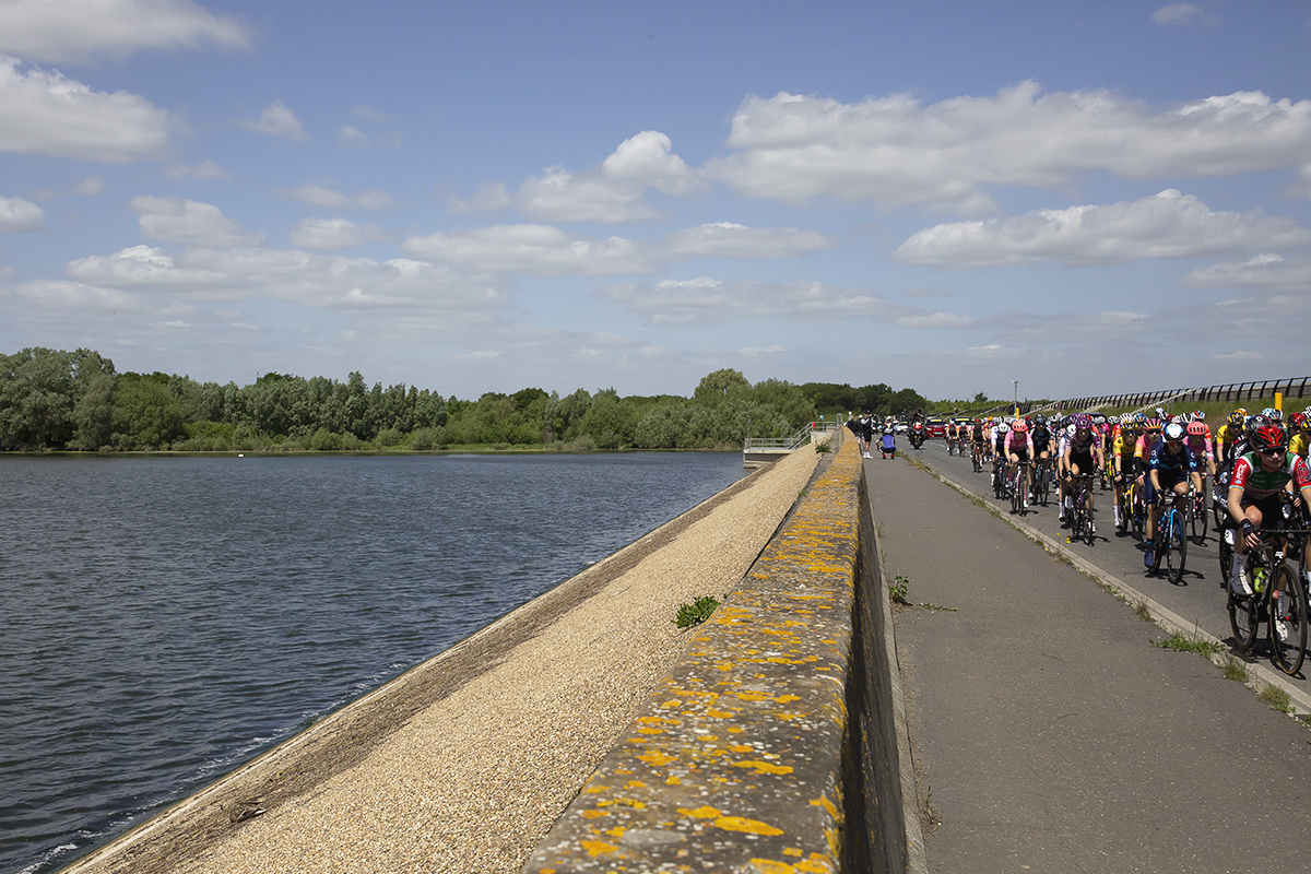 RideLondon Classique 2022 - The peloton ride over the dam at Abberton Reservoir, the dam wall in the foreground