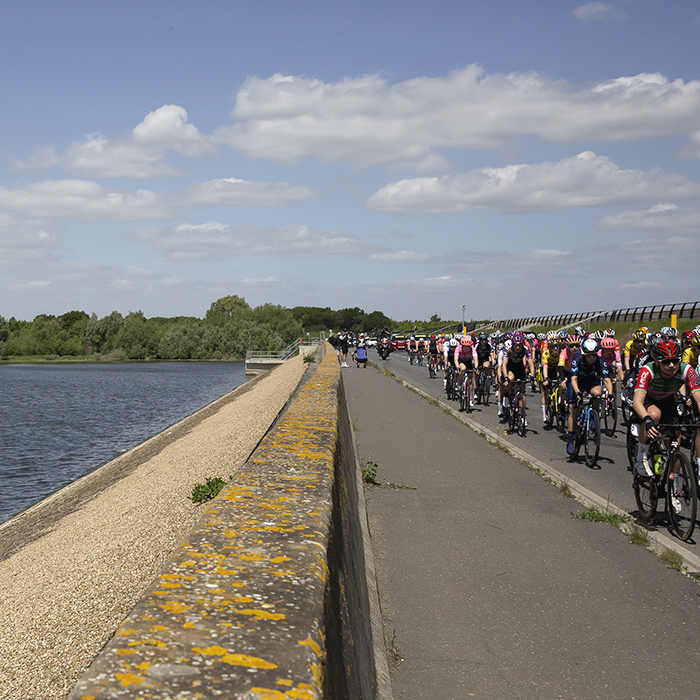 RideLondon Classique 2022 - The peloton ride over the dam at Abberton Reservoir, the dam wall in the foreground