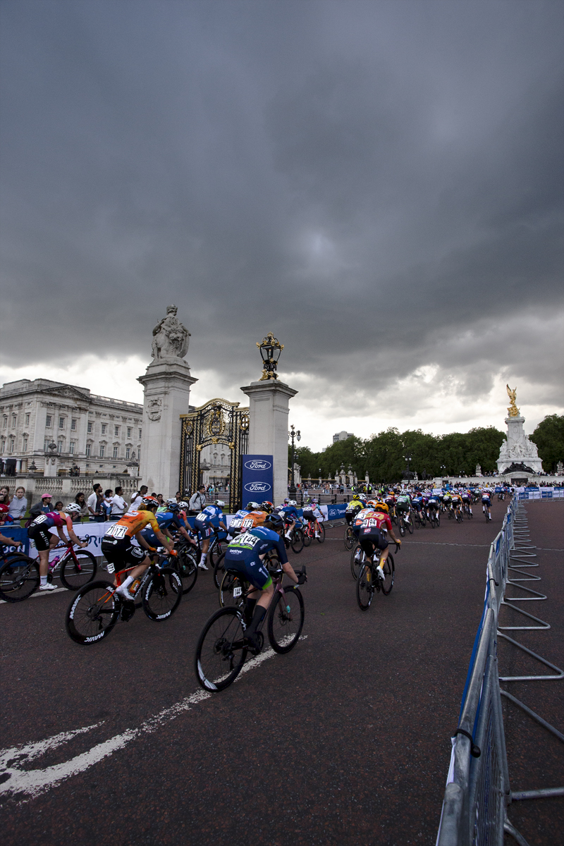 RideLondon Classique 2024 - The peloton passes by the ornate gates of Buckingham Palace under a stormy sky