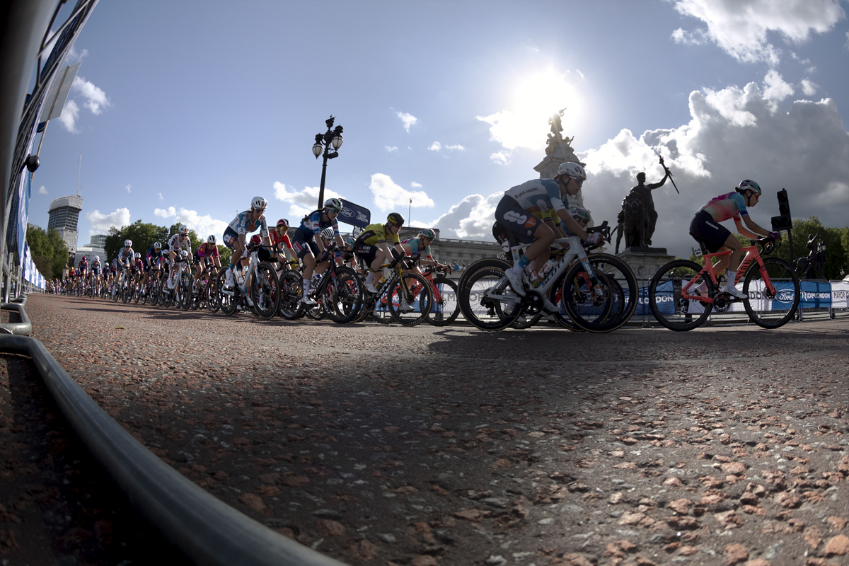 RideLondon Classique 2024 - The peloton pull onto The Mall in front of Buckingham Palace with the statues Winged Victory and Progress, parts of the Victoria Memorial, silhouetted against the sky