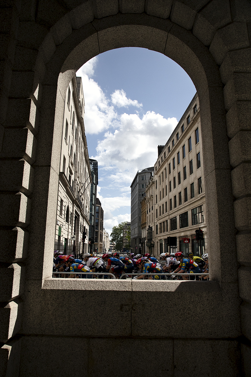 RideLondon Classique 2024 - The peloton seen through an archway on Cheapside in London