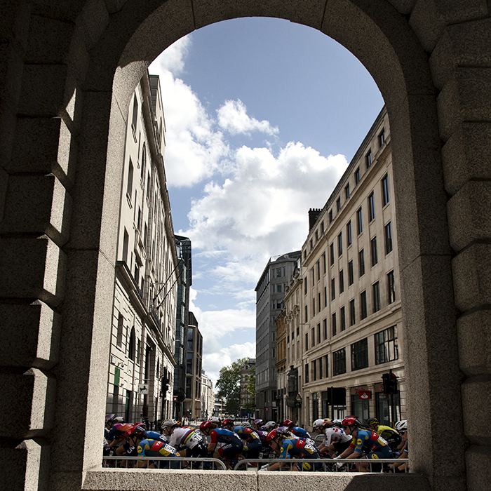 RideLondon Classique 2024 - The peloton seen through an archway on Cheapside in London