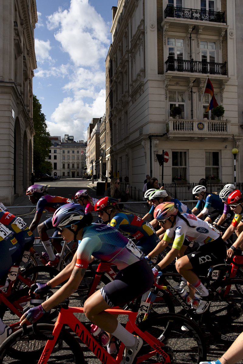 RideLondon Classique 2024 - The peloton on Pall Mall with grand stone buildings behind them