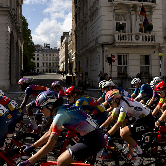 RideLondon Classique 2024 - The peloton on Pall Mall with grand stone buildings behind them