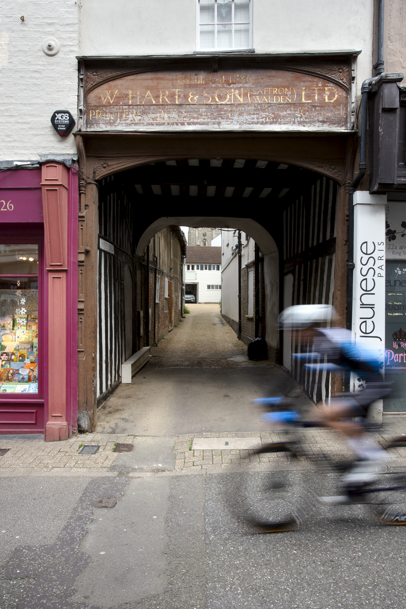 RideLondon Classique 2024 - A rider speeds past a wooden entrance in Saffron Waldon