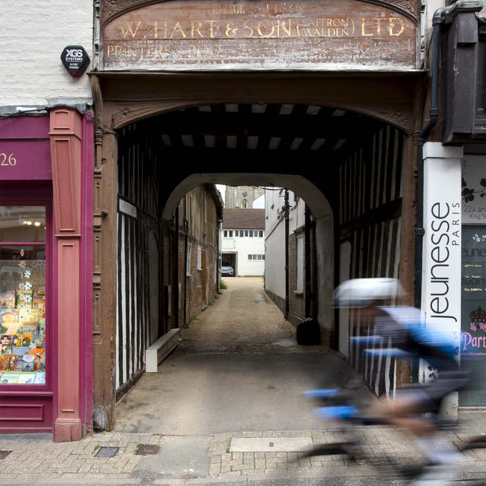 RideLondon Classique 2024 - A rider speeds past a wooden entrance in Saffron Waldon