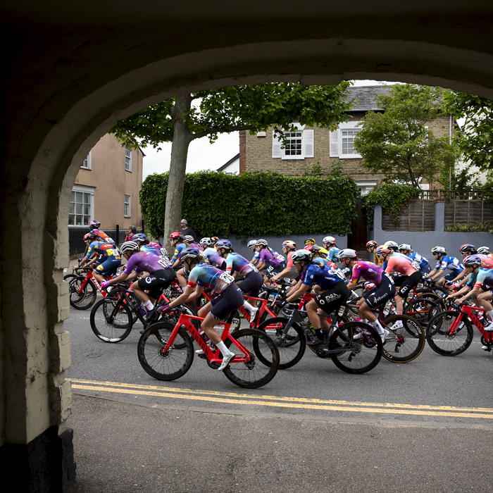 RideLondon Classique 2024 - The peloton seen through the entrance way of an old building