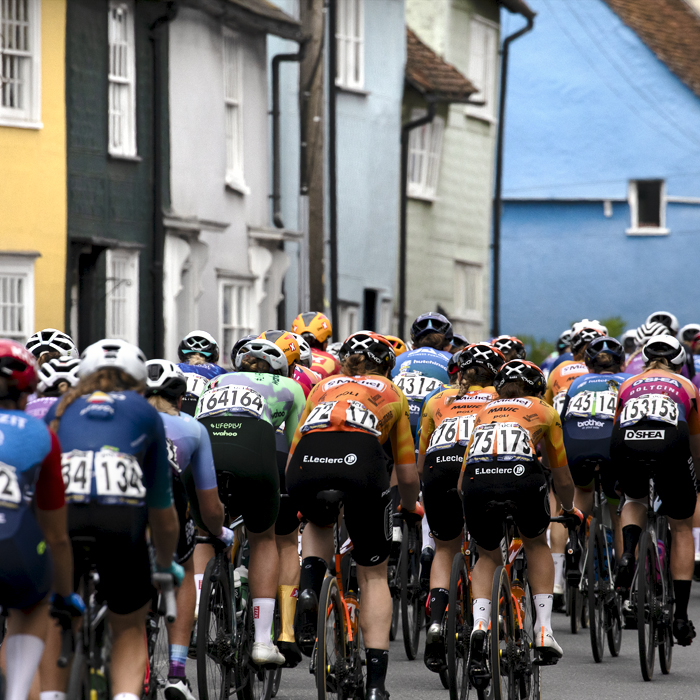 RideLondon Classique 2024 - The peloton moves away past brightly painted cottages