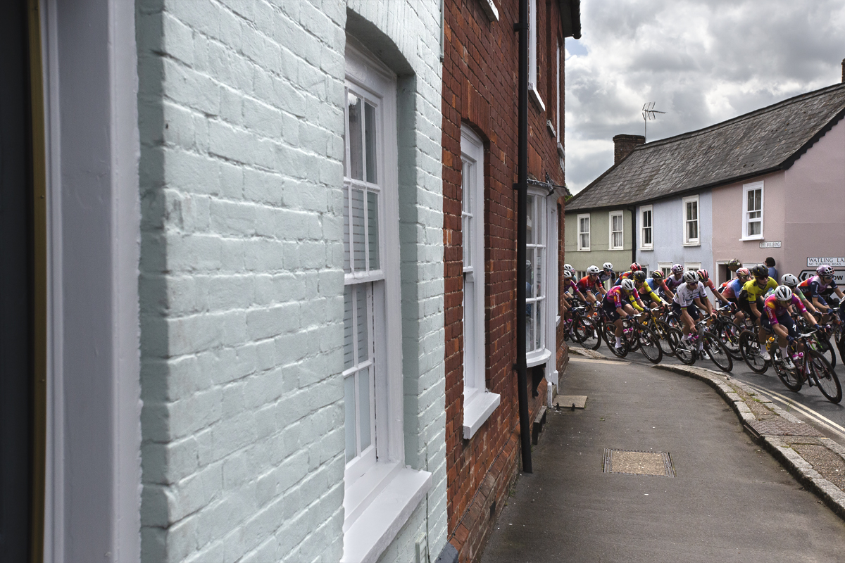 RideLondon Classique 2024 - The peloton rounds a corner past pastel coloured cottages in Thaxted