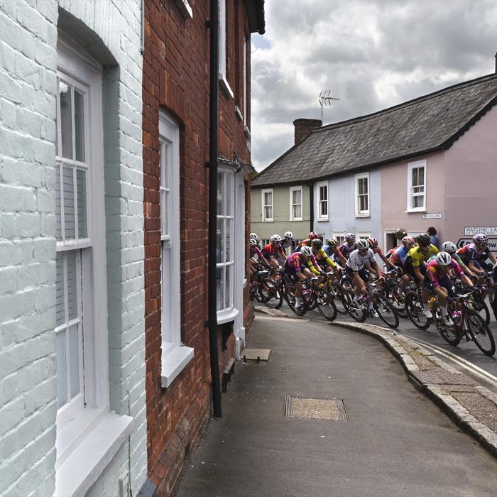 RideLondon Classique 2024 - The peloton rounds a corner past pastel coloured cottages in Thaxted