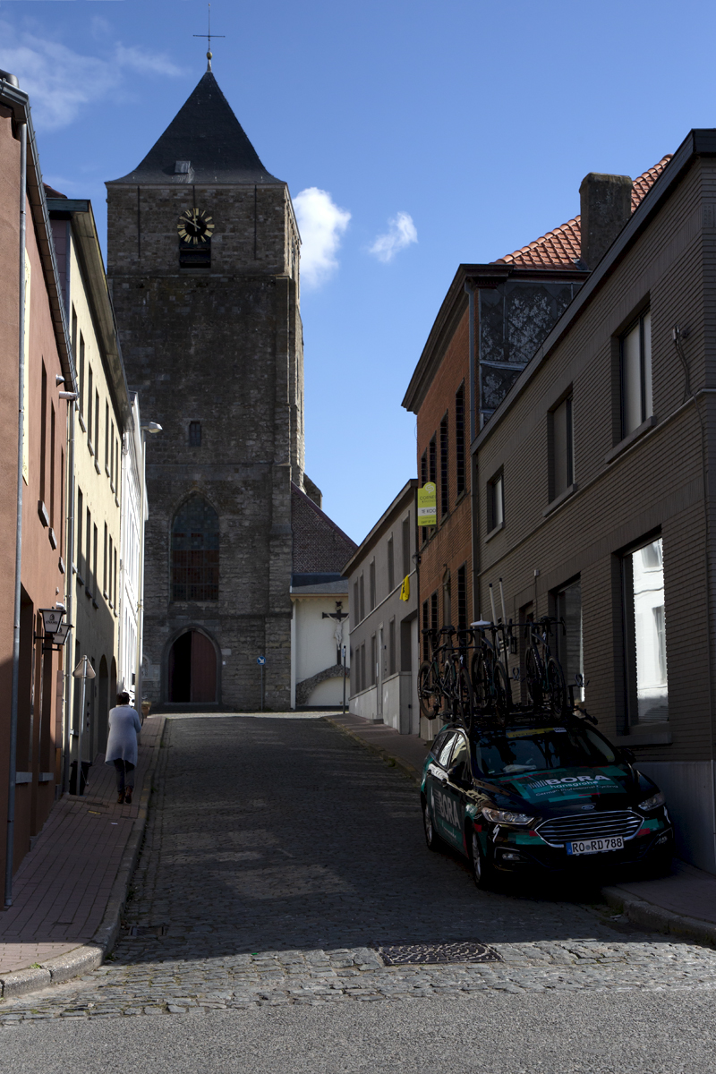 Ronde van Vlaanderen 2022 - A BORA - hansgrohe team car waits for the race in a cobbled side road beneath an old church