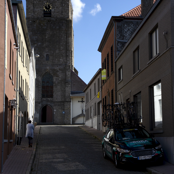 Ronde van Vlaanderen 2022 - A BORA - hansgrohe team car waits for the race in a cobbled side road beneath an old church