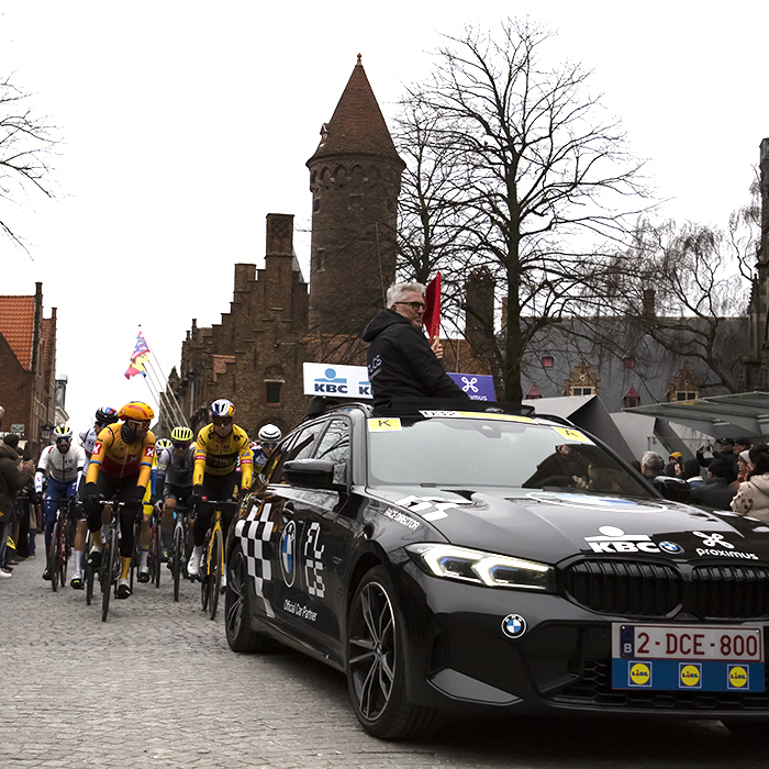 Ronde van Vlaanderen 2023 - The Race Director raises the flag out of the sunroof or his car at the neutral roll out in Brugge