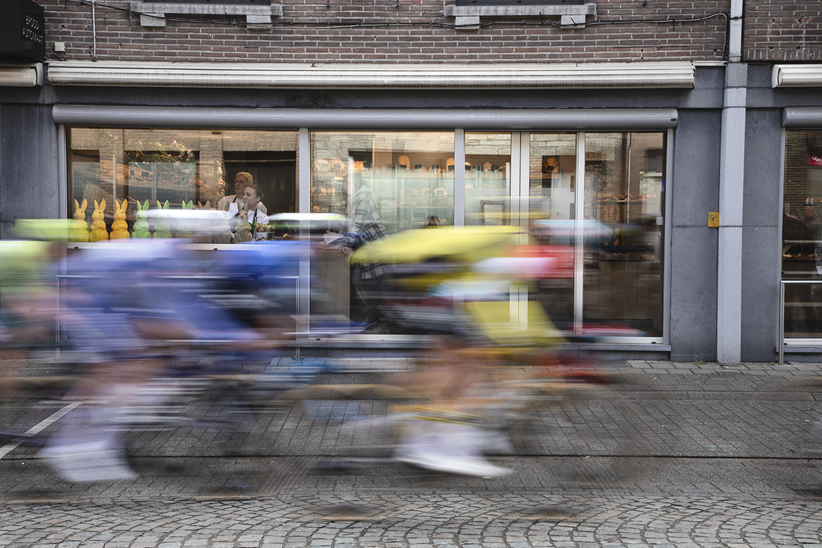 Ronde van Vlaanderen 2024 - Riders speed past a bakery as staff look out the windows past the Easter rabbits at the race