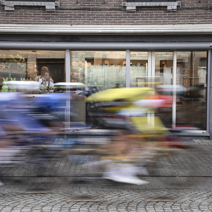 Ronde van Vlaanderen 2024 - Riders speed past a bakery as staff look out the windows past the Easter rabbits at the race