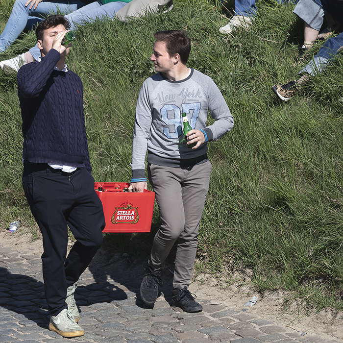 Ronde van Vlaanderen 2025 - Two young men carry a crate of Stella Artois and drink from bottles