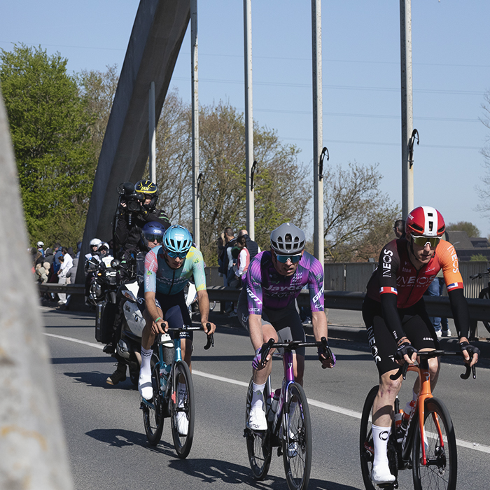Ronde van Vlaanderen 2025 - A small group of riders cross a modern arched bridge
