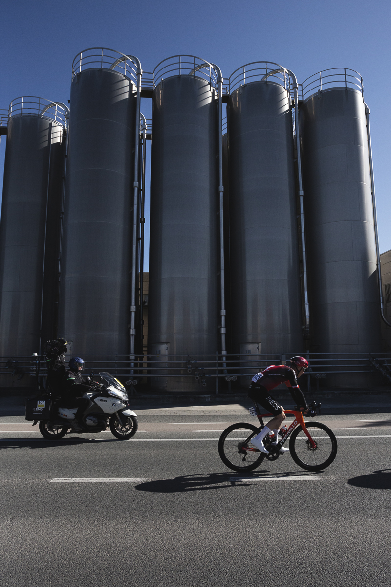 Ronde van Vlaanderen 2025 - Connor Swift rides past shiny industrial silos during the race
