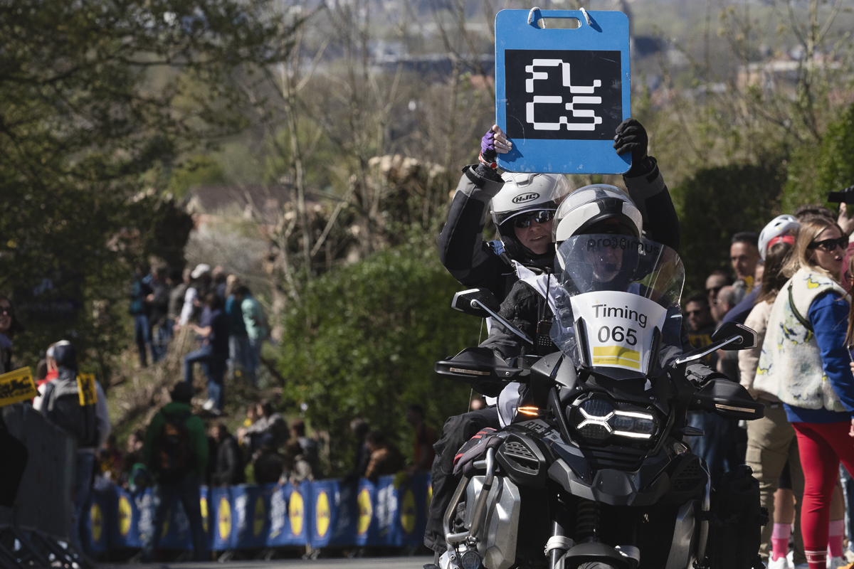 Ronde van Vlaanderen 2025 - The board indicating time splits is held aloft from the back of a motorbike