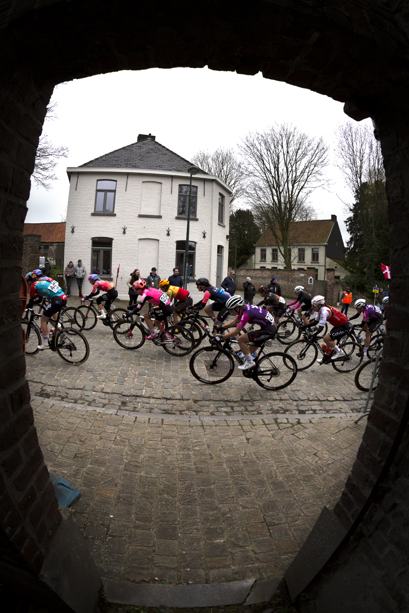 Ronde van Vlaanderen Vrouwen 2023 - The peloton seen through the doorway of a church in Wannegem Lede