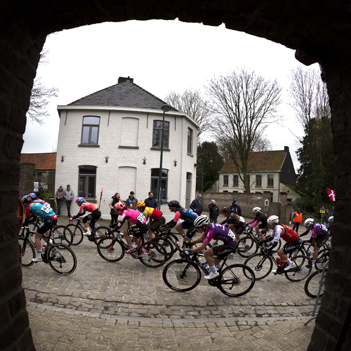 Ronde van Vlaanderen Vrouwen 2023 - The peloton seen through the doorway of a church in Wannegem Lede