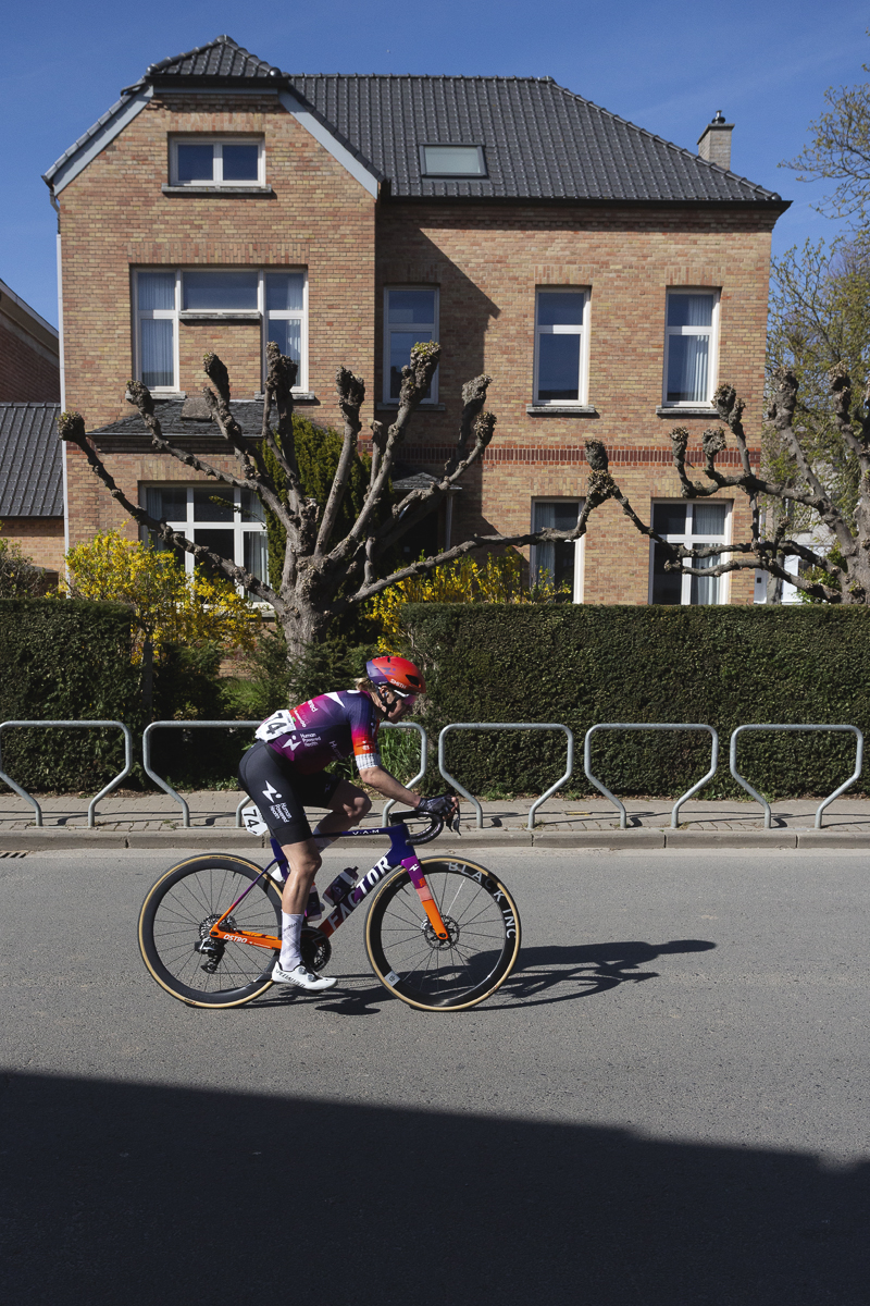 Ronde van Vlaanderen Vrouwen 2025 - Romy Kasper rides in front of a building with neatly pruned trees