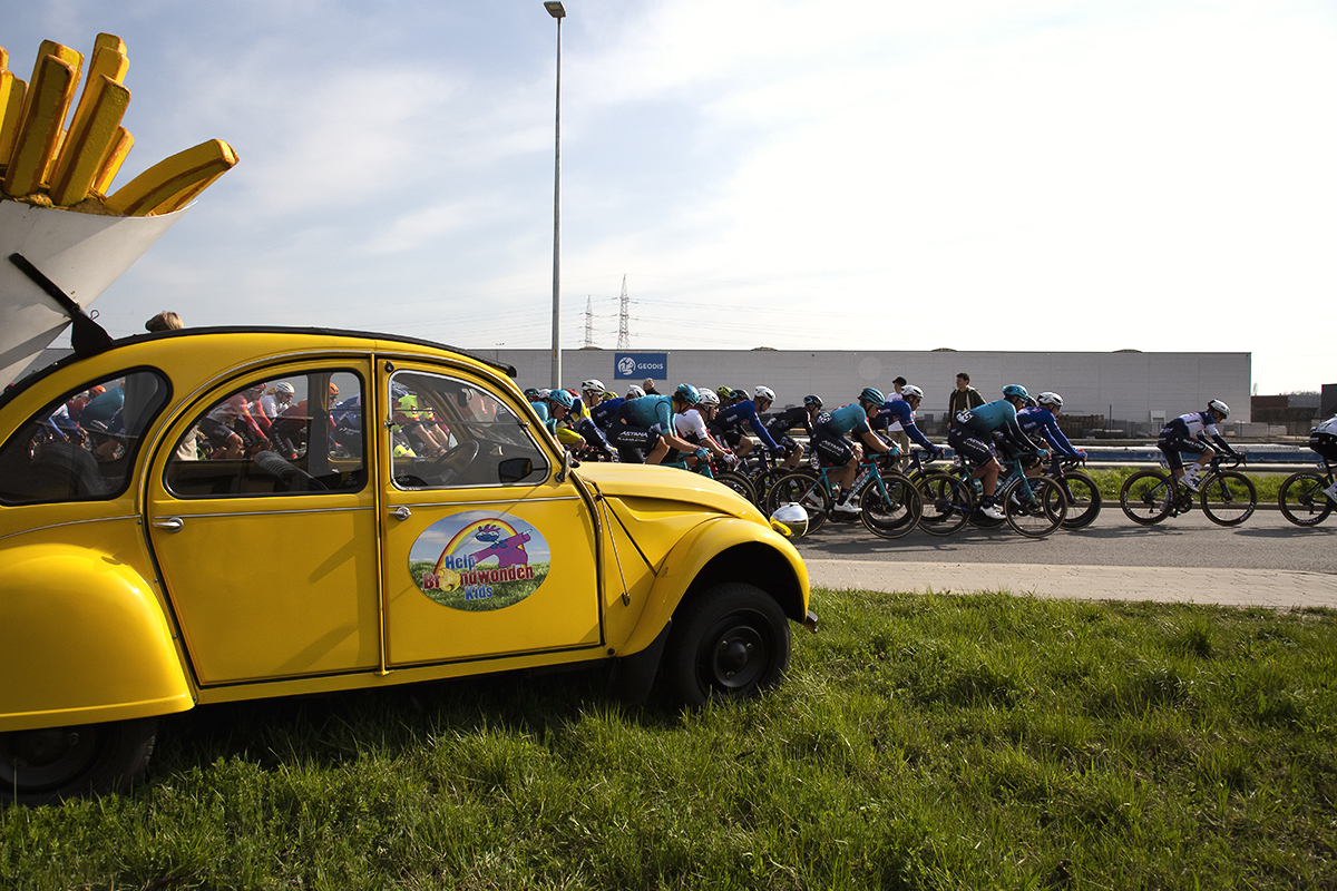 Scheldeprijs 2023 - The peloton passes a Citroen 2CV with a large model of a portion of frites fastened to its back