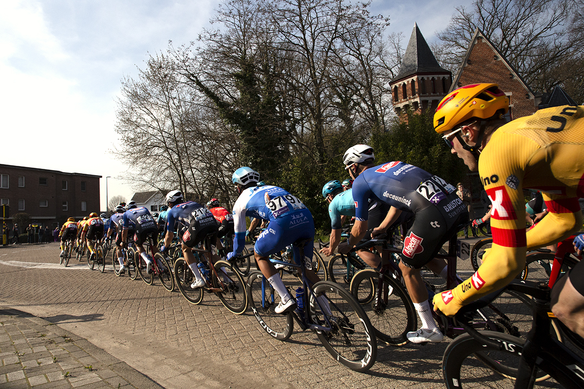 Scheldeprijs 2023 - The peloton hugs the inside of a bend as it passes a gatehouse to Kasteel Calesberg