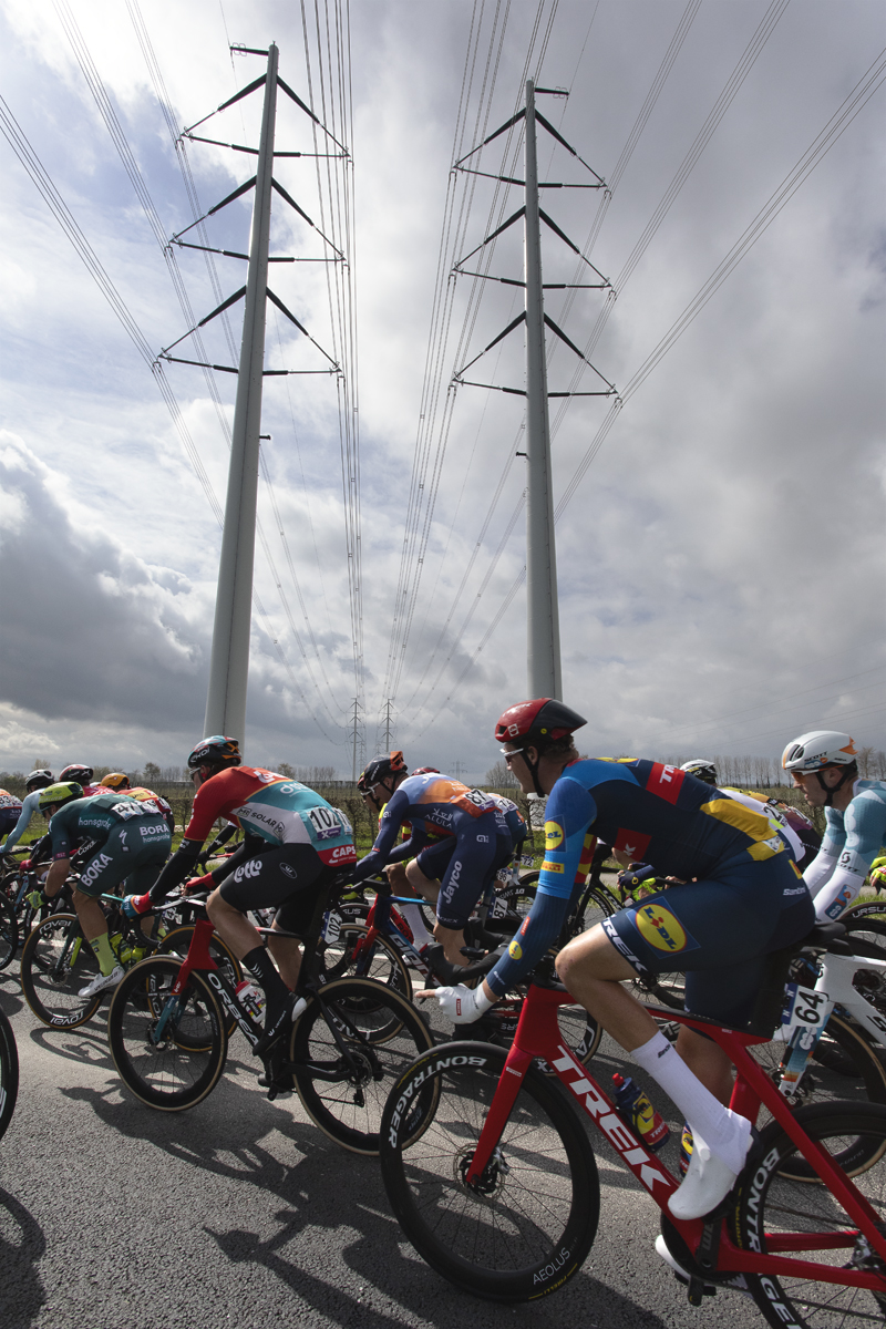 Scheldeprijs 2024 - Riders under a line of modern pylons near Heinkenszand