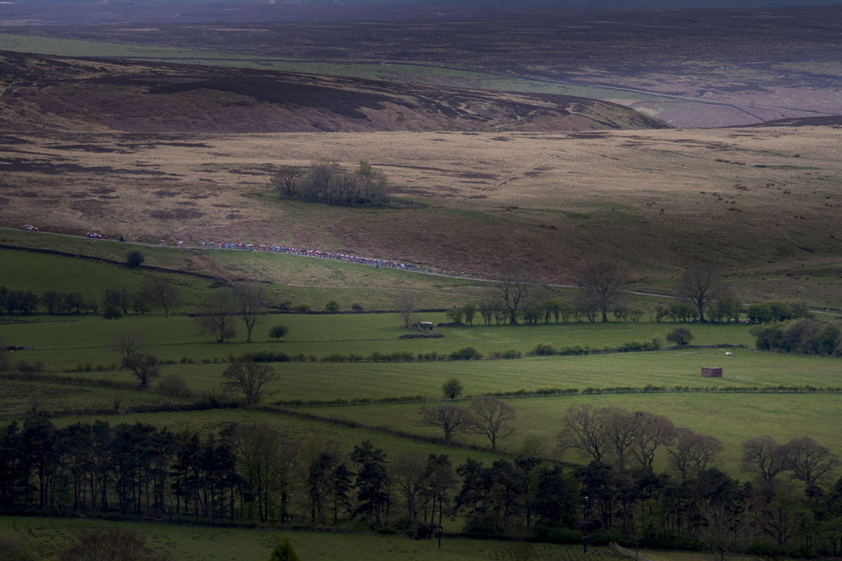 Tour de Yorkshire 2017 - the peloton is seen on a hill in the distance at Goathland