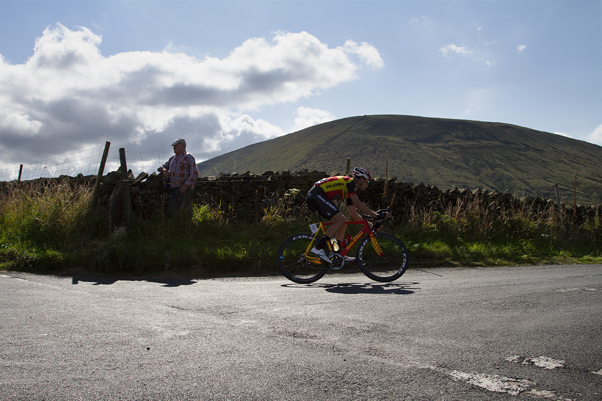 Tour of Britain 2015 - A rider passes an old man wearing a flat cap at the side of the road with the dominant feature of Pendle Hill in the background