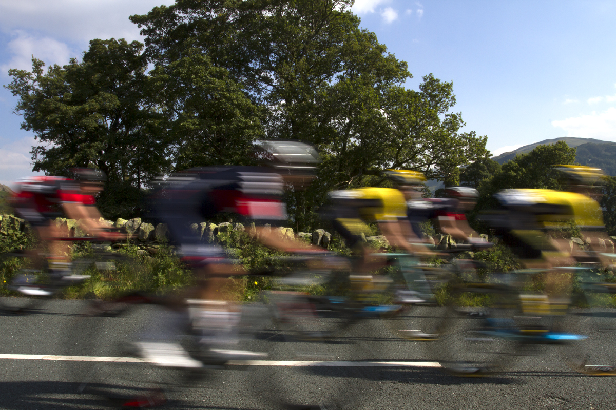 Tour of Britain 2015 - a group of riders with motion blur pass a dry stone wall and trees