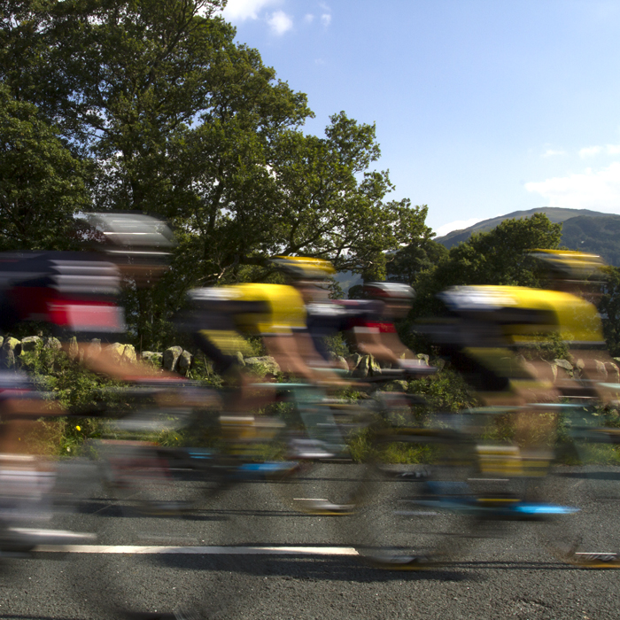 Tour of Britain 2015 - a group of riders with motion blur pass a dry stone wall and trees