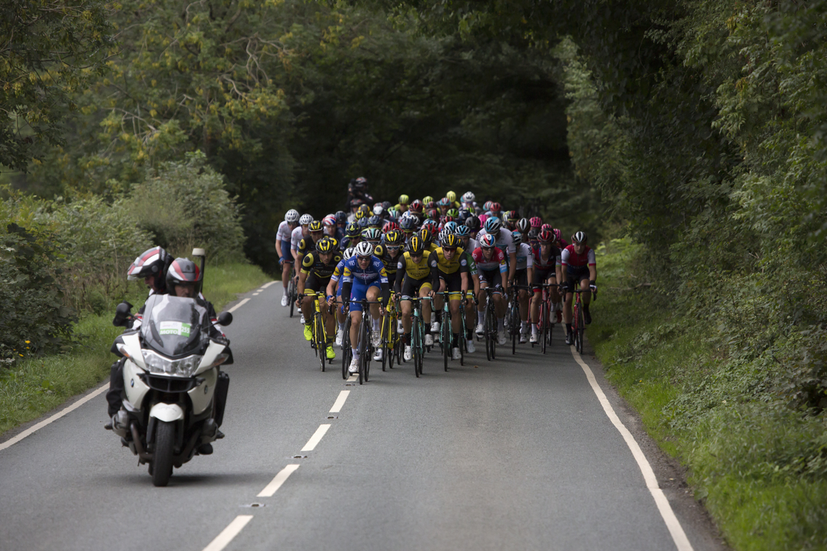 Tour of Britain 2018 - The peloton moves down tree lined roads in Cumbria