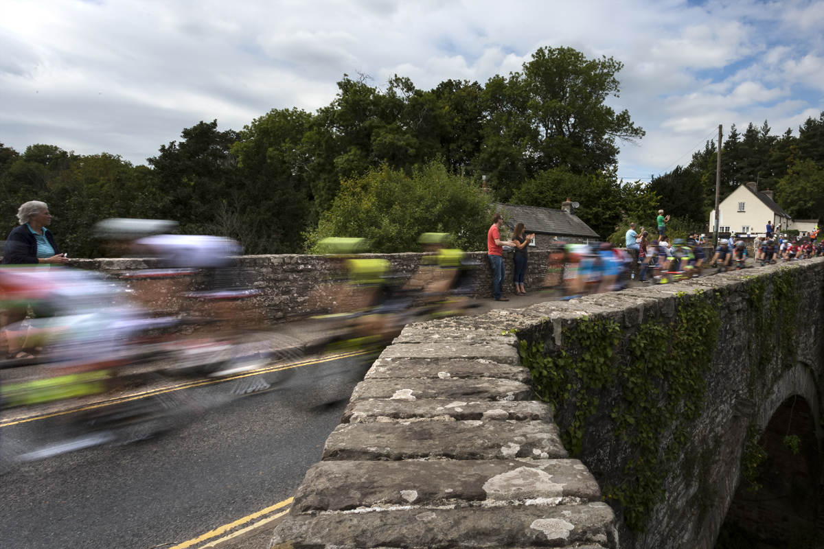 Tour of Britain 2018 - The peloton speeds over the bridge at Groesffordd