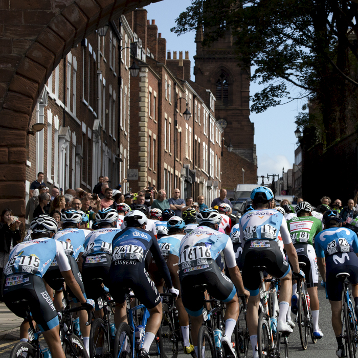 Tour of Britain 2019 - rear view of the  peloton passing under one of the gates in the walls in Chester